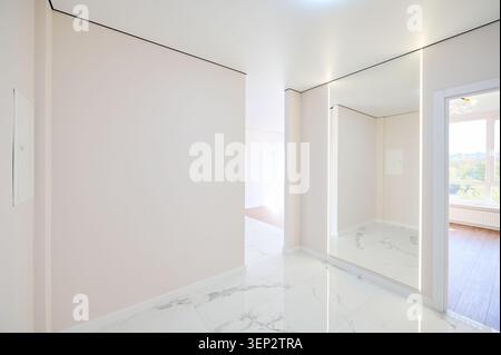 Geräumiger Wohnflur mit poliertem Fliesenboden, offenen Türen und beleuchteter Spiegelwand. Moderne Einrichtung der Apartments, elegante Renovierung und Immobilienkonzept Stockfoto