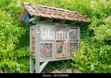 Ein großes handgefertigtes Holzinsektenhotel, das in einem grünen Garten in der Nähe von Büschen installiert ist. Fördert Biodiversität, ökologischen Gartenbau, Naturschutz und Öko Stockfoto