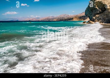 Schaumige Wellen, die auf die Sandküste des Strandes Agios Pavlos auf Kreta, Griechenland, Rollen. Pulsierendes türkisfarbenes Meer, umgeben von zerklüfteten Klippen unter einem klaren Medit Stockfoto