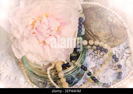 Vintage-Hintergrund mit rosa Pfingstrose, Juwelen im Glasgefäß und alter rostiger Eisenkugel auf der Spitze. Helles Leuchten. Stockfoto
