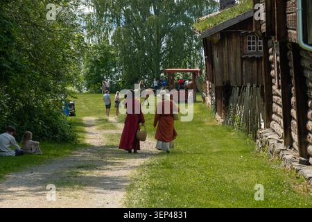 Zwei Frauen in mittelalterlich inspirierter Kleidung spazieren während eines mittelalterlichen Festivals in Hamar, Norwegen, auf einem Schotterweg zwischen historischen Gebäuden Stockfoto