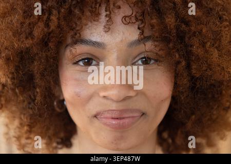 Direkt in die Kamera blickend, Frau Mitte 20, zeigt lockiges Haar, Lippenglanz, Creolen-Ohrring im Studio Stockfoto