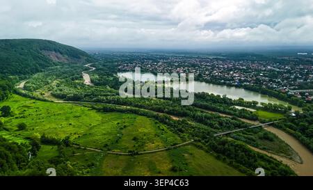 Der hohe Aussichtspunkt zeigt einen sich windenden Fluss und Seen neben einer wachsenden Stadt. Grüne Auen und bewaldete Hügel säumen Viertel und Brücken. Balanced sc Stockfoto