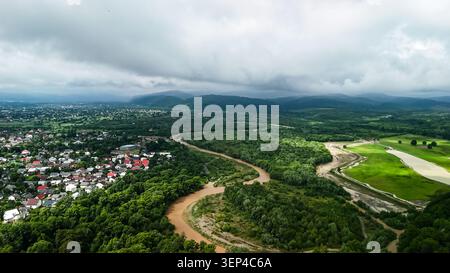 Herrlicher Blick auf einen sich windenden Fluss, der durch dichte grüne Tiefländer in Richtung entfernter Berge schneidet. Wolken hängen tief, während verschiedene Kanäle schimmern. Eine vibra Stockfoto