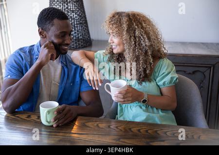 Verschiedene Paare sitzen zu Hause Esstisch mit Keramikbecher mit Lampe auf Sideboard dahinter Stockfoto