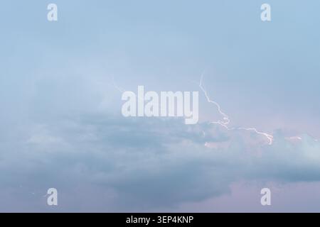Ein beeindruckendes Bild, das einen starken Blitz aufnimmt, der die dunklen, stürmischen Wolken vor einem blassblauen und violetten Abendhimmel beleuchtet und das R zeigt Stockfoto