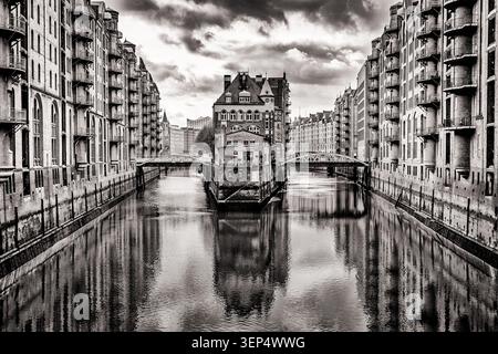 Schwarz-weiß-Blick auf das historische Wasserschloss, das sich in einem Kanal in Hamburgs zum UNESCO-Weltkulturerbe gehörender Speicherstadt spiegelt. Stockfoto