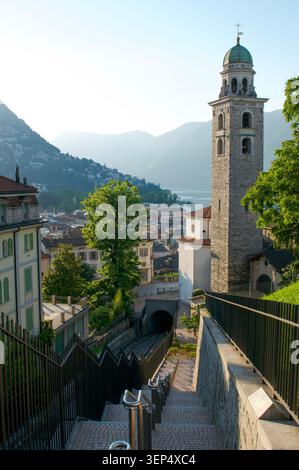 Malerischer vertikaler Blick von der Spitze der Treppe am Bahnhof Lugano mit der Kathedrale San Lorenzo und ihrem Glockenturm im Vordergrund, mit dem Stockfoto