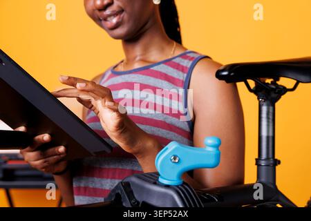 Detaillierte Ansicht einer Jugendlichen schwarzen Frau, die auf ihrem Smartphone-Tablet nach Fahrradwartung sucht. Nahaufnahme einer afroamerikanischen Radfahrerin mit einem intelligenten Gerät, während sie ihr Fahrrad untersucht. Stockfoto