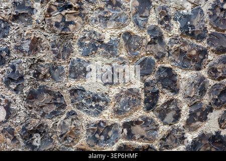 Eine Steinmauer aus Feuerstein in verschiedenen Formen und Größen. Die Steine sind grau und schwarz, in einem hellen Mörtel. Das Bild erfasst den Stockfoto