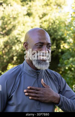 Ranghoher Afroamerikaner lächelt im Park, hält die rechte Hand in grauer Reißverschlussjacke über der Brust Stockfoto