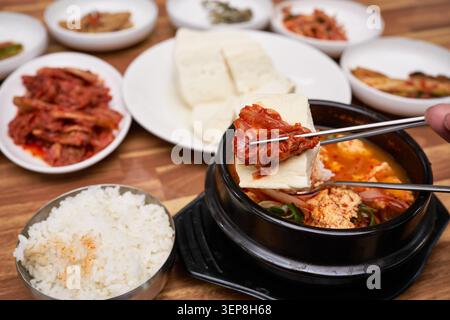 Scharfer, weicher Tofu-Eintopf in einem heißen Steintopf, zusammen mit geschnittenem Tofu und Kimchi auf einem Holztisch Stockfoto