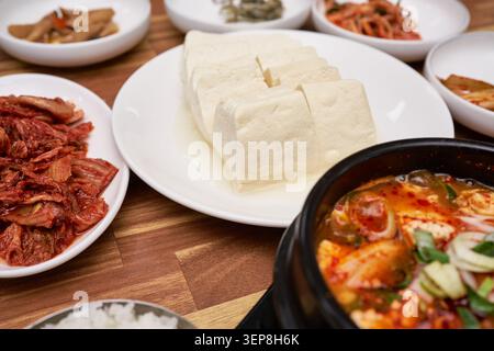 Scharfer, weicher Tofu-Eintopf in einem heißen Steintopf, zusammen mit geschnittenem Tofu und Kimchi auf einem Holztisch Stockfoto