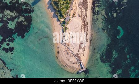 Dieses atemberaubende Bild aus der Luftaufnahme zeigt eine ruhige tropische Strandlage mit einer sandigen Küste, die sich um eine ruhige türkisfarbene Lagune dreht. Ein Wald Stockfoto