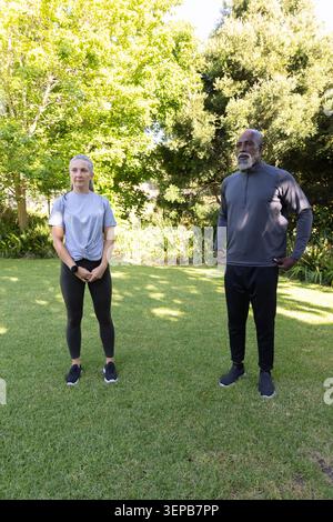 Erwachsene Frau und Senior Mann stehen im Garten mit Sportbekleidung und Turnschuhen Frau zeigt Tracker Stockfoto