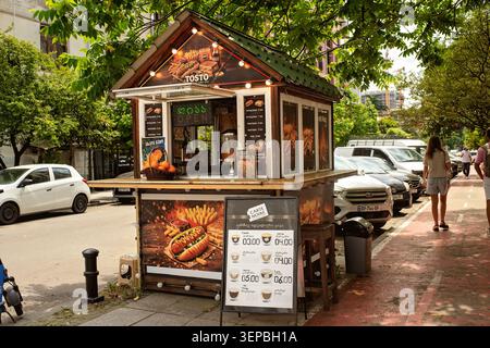 Batumi, Georgia - 9. Juni 2026: Eine Stadtstraße mit einem kleinen hölzernen Fast-Food-Kiosk mit hellen Werbeanzeigen für Hot Dogs, Sandwiches und Kaffee Stockfoto