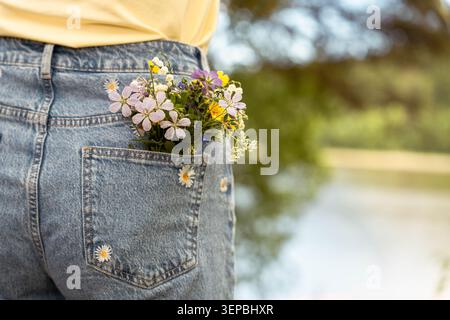 Nahaufnahme aus Denim-Jeans mit einem kleinen Blumenstrauß in der Gesäßtasche, vor einem weich verschwommenen Outdoor-Hintergrund mit warmem Hintergrund Stockfoto
