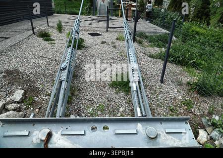 Nahaufnahme von Drahtseilen aus robustem Stahl und Spannankern, die eine moderne Fußgängerbrücke auf einem Kiesboden sichern. Ideal für Stockfoto