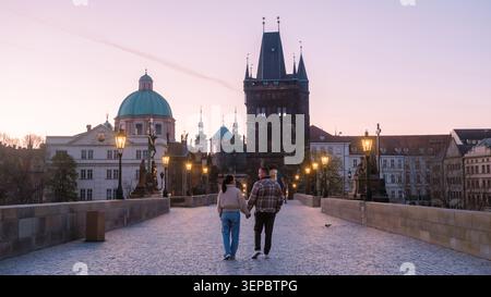 Ein paar Spaziergänge Hand in Hand auf der historischen Karlsbrücke in Prag, wenn die Sonne untergeht. Die charmante Architektur und das sanfte Leuchten der Lampen schaffen eine magische Atmosphäre für Touristen und Einheimische gleichermaßen. Stockfoto