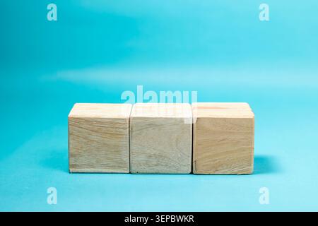 Drei leere, einfache Holzblockwürfel, die in einer horizontalen Linie eng aneinander angeordnet sind, vor einem leuchtenden türkisblauen Hintergrund, bereit für die Platzierung von benutzerdefiniertem Text oder Logo. Hochwertige Fotos Stockfoto