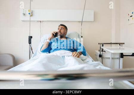 Reifer Mann empfängt Telefonanruf im Krankenhausbett Stockfoto