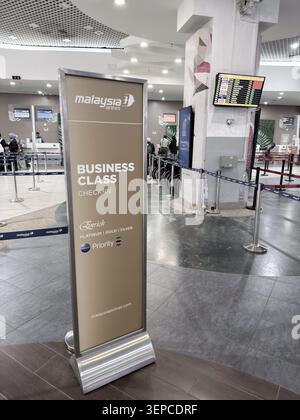 Penang, Malaysia - 28. April 2025: Das Check-in-Schild für die Business-Klasse steht an prominenter Stelle. Die Fluginformationstafel bietet Updates. Stockfoto