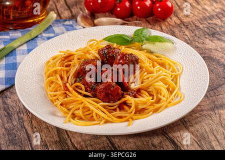 Herzhafte Spaghetti mit herzhaften Fleischbällchen in reichhaltiger Tomatensauce, garniert mit frischem Basilikum. Auf rustikalen Holztisch mit Tomaten, Knoblauch, Zwiebeln, o Stockfoto