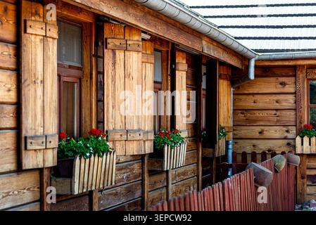 Traditionelles Holzhaus mit rustikalen Fenstern, Schutzläden und leuchtend roten Geranien in Fensterkästen Stockfoto