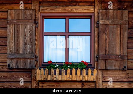 Hölzerne Hausfassade mit einem Fenster mit rustikalen Fensterläden und Blumenkasten mit roten Geranien Stockfoto
