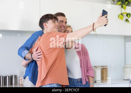 Familie Dreiereltern und Sohn lehnten sich ein, lächelten und machten Selfie in der modernen Küche mit Smartphone Stockfoto