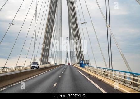 Eine Nahaufnahme mit symmetrischen Aufnahmen, die die monumentalen Betonmasten und das dichte Netz von Stahlseilen auf der Normandie-Brücke zeigen. Einige Fahrzeuge tr Stockfoto