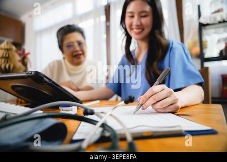Nahaufnahme Krankenschwester Hand schreibt medizinische Aufzeichnung Clipboard Haus, lächelnde asiatische Krankenschwester in blauen Schürfkübeln schreibt Notizen mit Stift, füllt Checkliste älterer Patient, Stockfoto