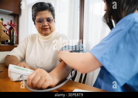 Asiatische Seniorin erhält Blutdruck-Check-Arzt während junge Krankenschwester mit digitalem Sphygmomanometer Senioren, Altenpflegungs-Service Routi Stockfoto