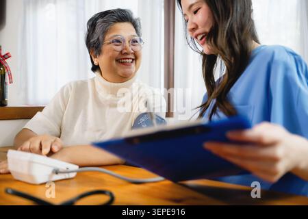 Asiatische ältere Frau lächelt, während Krankenschwester medizinische Ergebnisse zeigt, häusliche Pflege Pflege Pflege zeigt Clipboard zufriedene ältere Patienten, ältere Frau empfangen Stockfoto