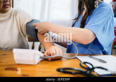 Medizinisches Fachpersonal misst Blutdruck. Sie trägt eine blaue Uniform. Die ältere Frau entspannt ihren Arm. Ihr Ausdruck ist ruhig und kooperativ. Stockfoto