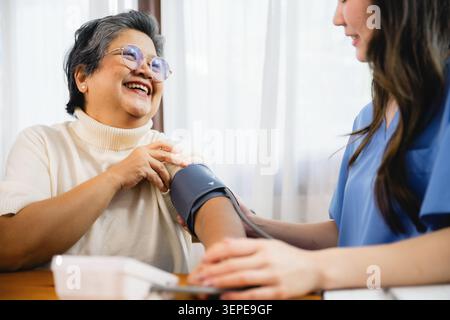 Frau lächelt, während ihr Blutdruck gemessen wird. Sie trägt einen leichten Pullover und sieht entspannt aus. Die Schwester in blauen Schutten konzentriert sich auf die Aufgabe. Sie sitzen bei Stockfoto