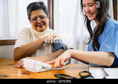 Die junge Krankenschwester überprüft den Blutdruck der Senioren mit einem digitalen Sphygmomanometer. Seniorin lächelt herzlich über die Interaktion im Gesundheitswesen. Schwester zeigt Ruhe, prof Stockfoto