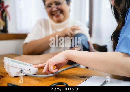 Nahaufnahme der Schwester, die auf die Anzeige des Blutdruckmessgeräts zeigt. Ruhige Hände halten den Arm des Patienten mit der Manschette. Der Patient lächelt und zeigt Vertrauen in die Pflege. Klinisch Stockfoto