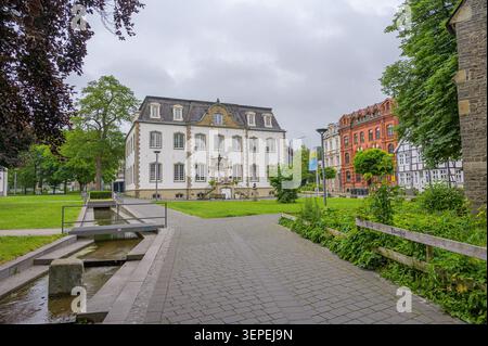 Iserlohn, Deutschland - 05. Juni 2026: Historische Gebäude, Parkgelände, Bach, gepflasterter Weg unter bewölktem Himmel. Stockfoto