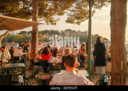 Menschen genießen den Sonnenuntergang und den Panoramablick auf das historische Alfama-Viertel und den Tejo-Fluss von einem beliebten miradouro in Lissabon, Portugal. Stockfoto