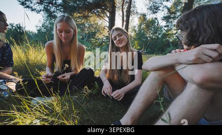 Freunde im Teenageralter entspannen sich auf grasbewachsenem Boden, verbinden sich und lachen während der Freizeit im Freien Stockfoto
