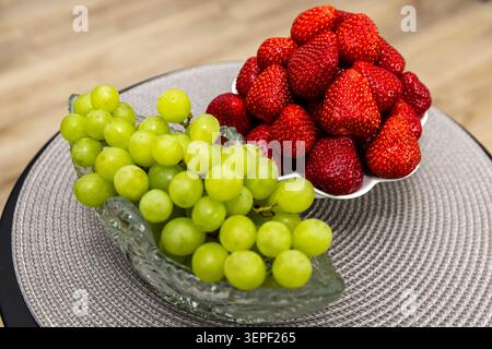Frische grüne Trauben und reife Erdbeeren werden in eleganten Schüsseln präsentiert und bieten eine gesunde und farbenfrohe Auswahl an saisonalen Früchten. Stockfoto