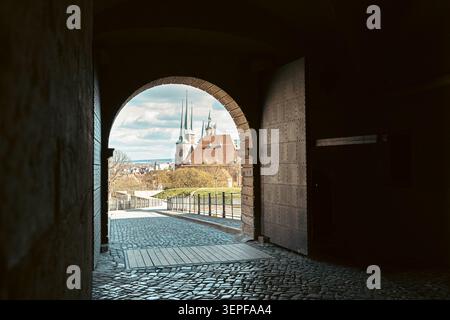 Erfurt, Deutschland - 27. März 2026. Blick auf den Erfurter Dom erhebt sich durch eine dunkle bogenförmige Passage an der Petersberg Zitadelle mit Kopfsteinpflaster und Hi Stockfoto