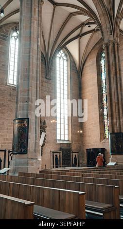 Erfurt, Deutschland - 27. März 2026. Vertikaler Blick in eine gotische Kirche mit hohen Buntglasfenstern, geriffelten Gewölben, Steinsäulen, Holzbänken, rel Stockfoto