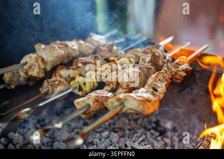 Gegrillte Fleischspieße, Die Über Offenem Feuer Kochen. Metallspieße mit gegrilltem Fleisch und geschnittenem Gemüse kochen über heißer Holzkohle neben hellen Flammen. Stockfoto