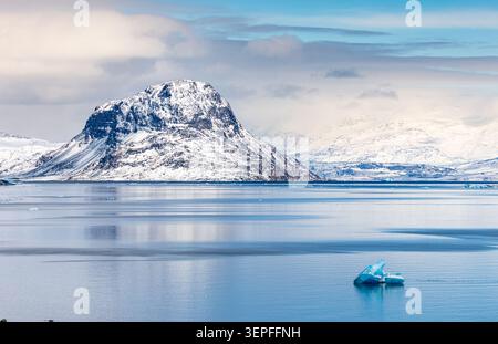 Schneebedeckte Berge spiegeln sich in ruhigem Fjordwasser mit einem blauen Eisberg in der Nähe von Narsaq, Kujalleq, Grönland Stockfoto