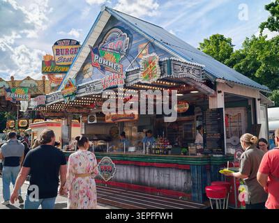 Pforzheim Deutschland - 14. Juni 2026 Ein belebter Karnevalsstand im Freien, dekoriert mit farbenfrohen Vintage-Schildern und Festzelt-Lichtern. Das hölzerne k Stockfoto
