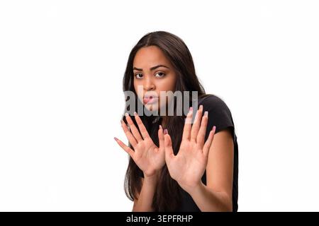 Verängstigte und schockierte junge hispanische Frau, die zurücktritt und beide offene Handflächen in einer Defensive oder Weigerung hält. Studio-Aufnahme, die f darstellt Stockfoto