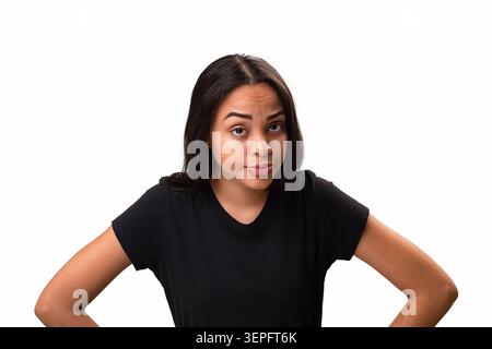 Zweifelnde und misstrauische junge hispanische Frau, die in die Kamera blickt, Hände auf den Hüften und einen fragenden Gesichtsausdruck. Studio-Aufnahme, die di darstellt Stockfoto