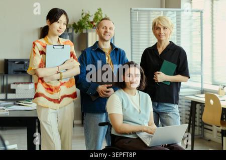 Porträt verschiedener junger erwachsener Kollegen, die mit Laptop und Dokumenten im Büro posieren und Teamarbeit und Integration repräsentieren. Ideal für Arbeitsplatzkultur, Personalwesen und Recruiting-Kampagnen Stockfoto